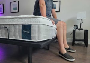 Side view of a man sitting on the edge of a Leesa Sapira Chill hybrid mattress.