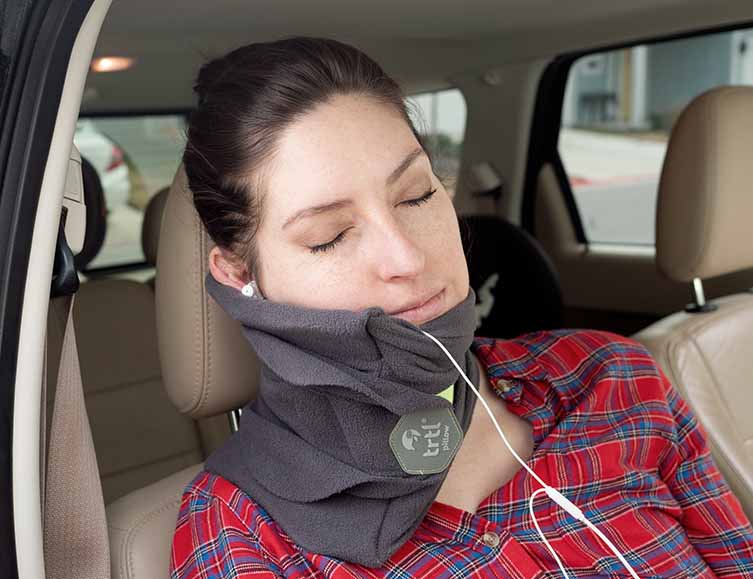 A woman sleeps in the car with the trtl pillow.