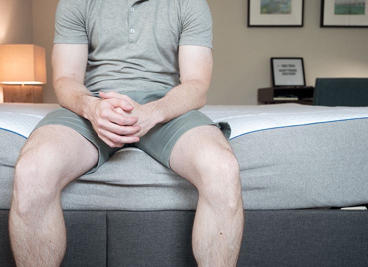 A man sits near the edge of a mattress.
