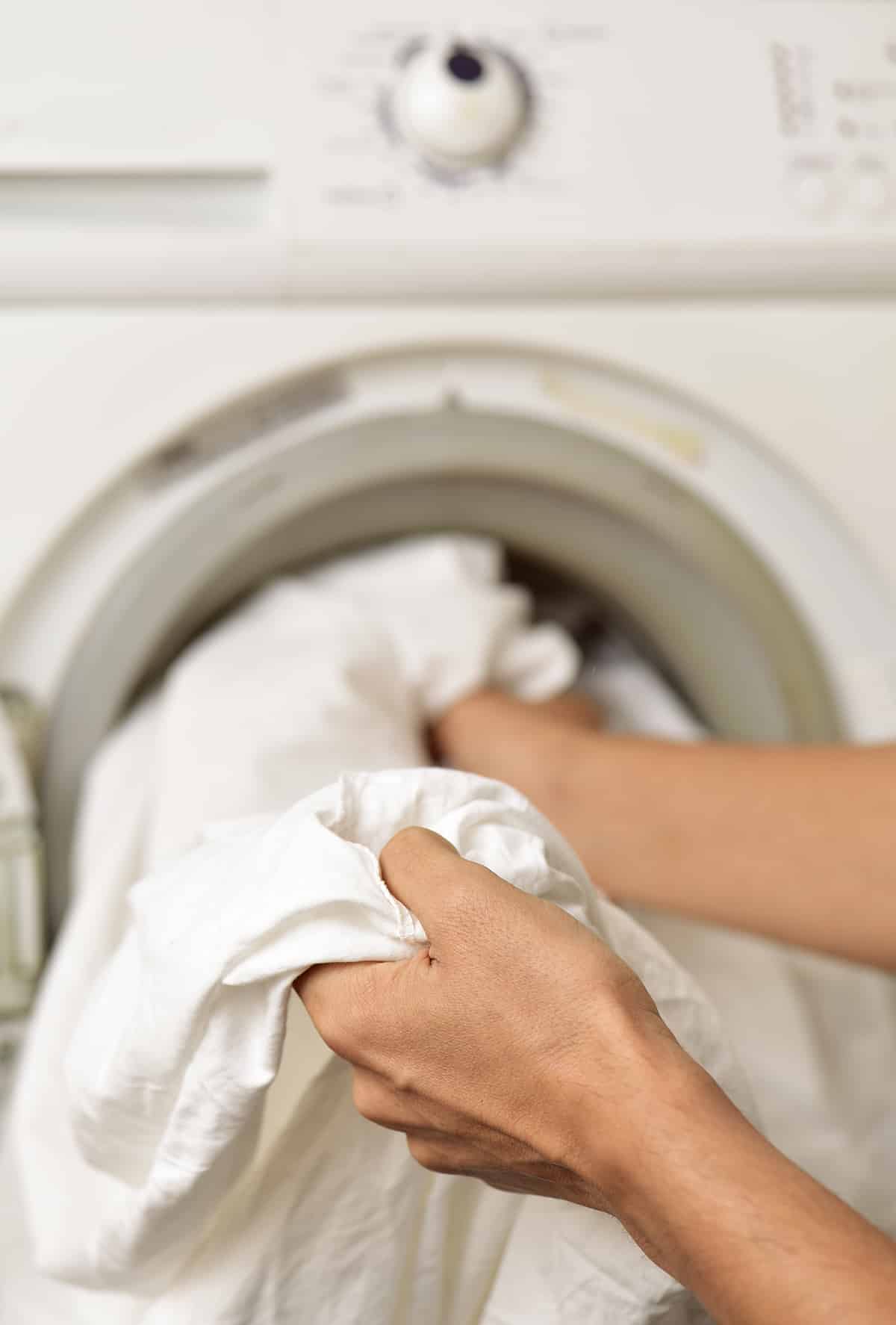 Hands putting sheets into a washing machine.