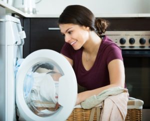 A woman putting sheets into a washing machine.