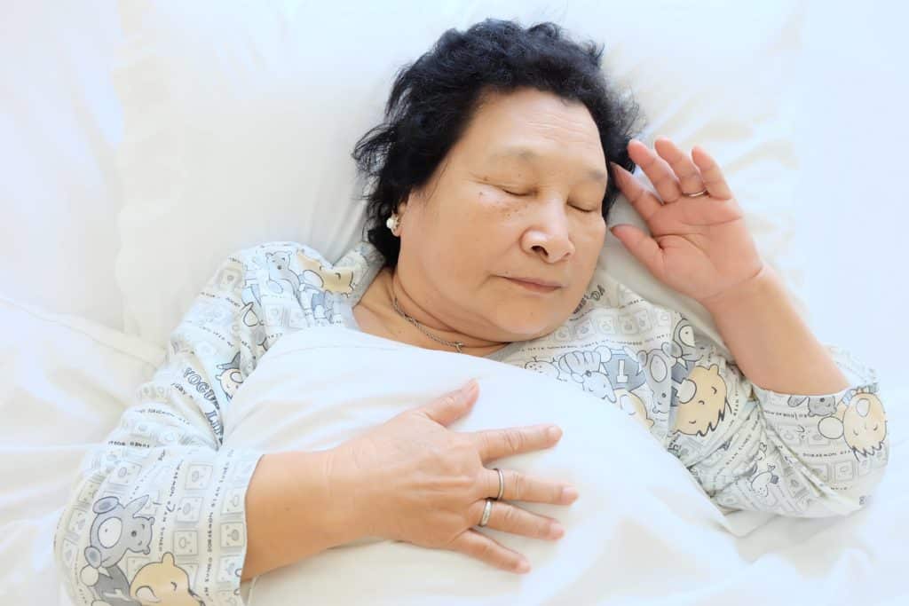 An older woman sleeps in a bed under the covers