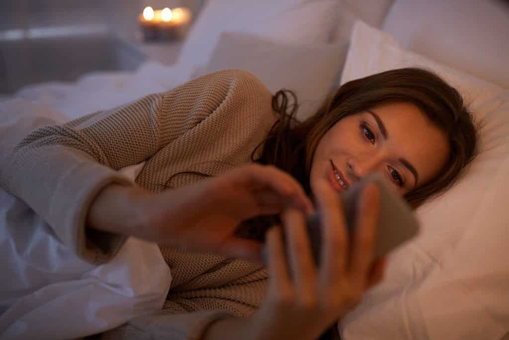 A woman looks at her phone before bed