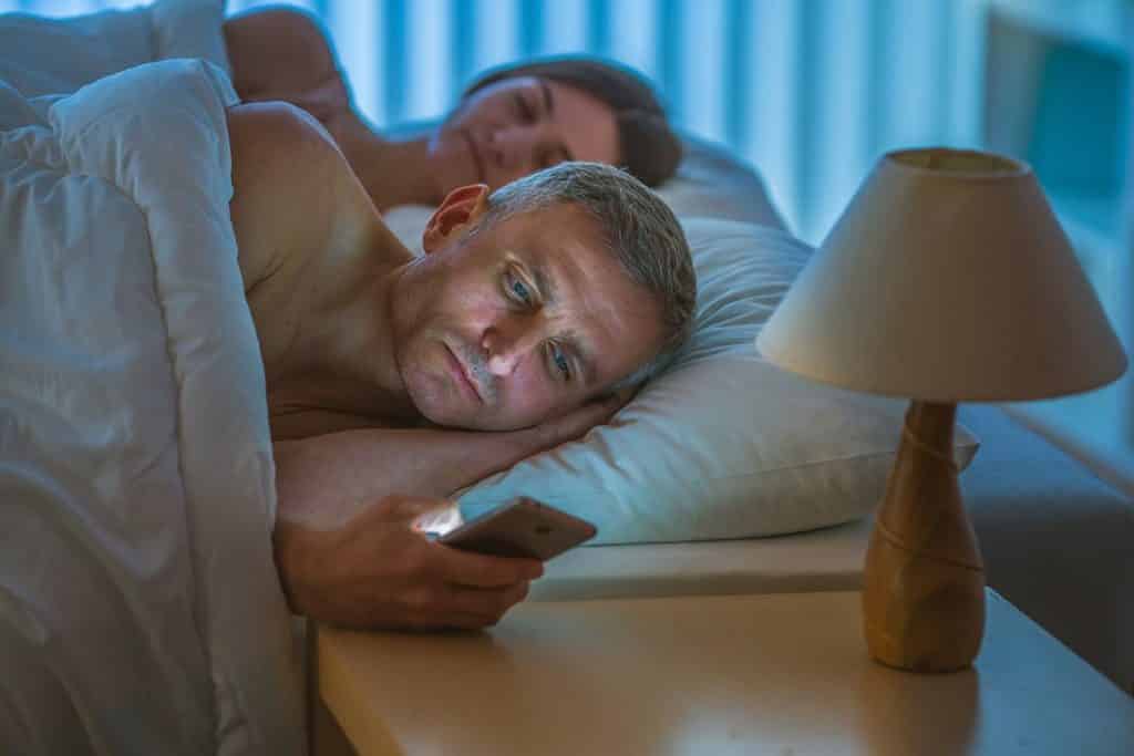 A man texts on his phone from bed