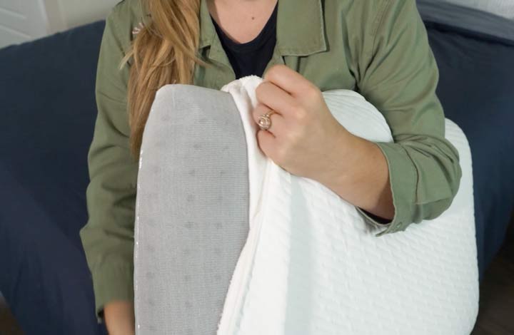 A woman pulls back the outer cover of the Tuft & Needle Original foam pillow.