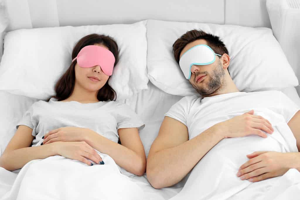 a couple sleeps with eye masks on in a bed