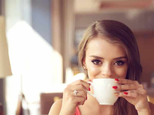 A smiling girl drinks coffee.