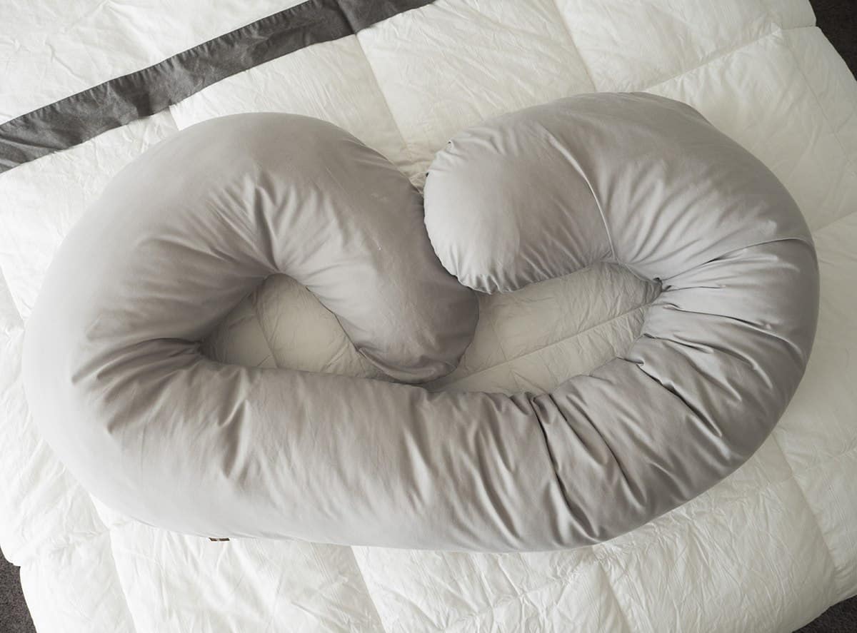 The Leachco Snoogle Body Pillow with the gray jersey cover rests on top of a white comforter.