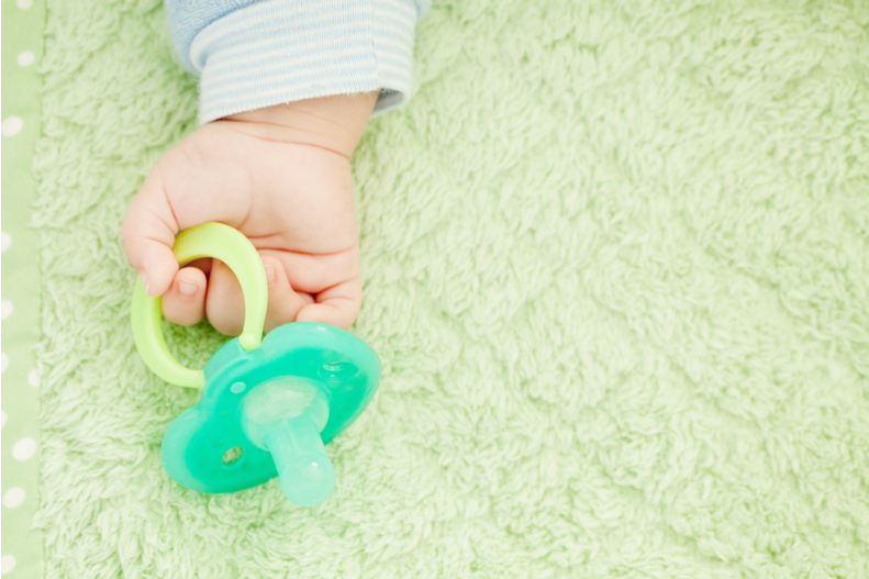 A child's hand holding a pacifier.