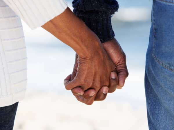 Two people hold hands on the beach.