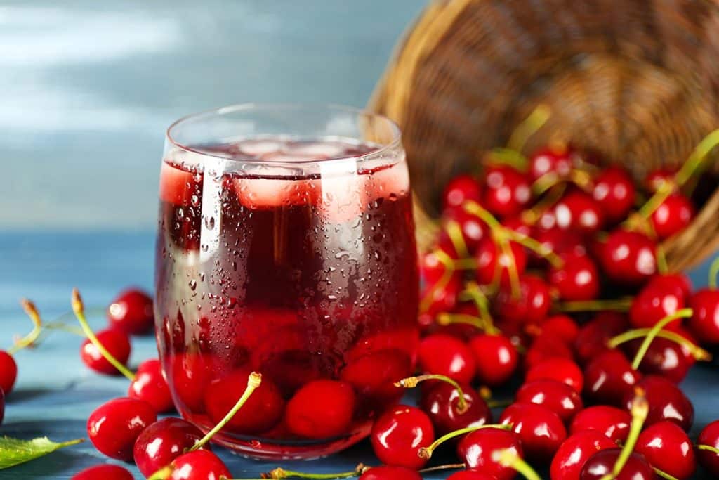 A cup of tart cherry juice surrounded by fresh cherries