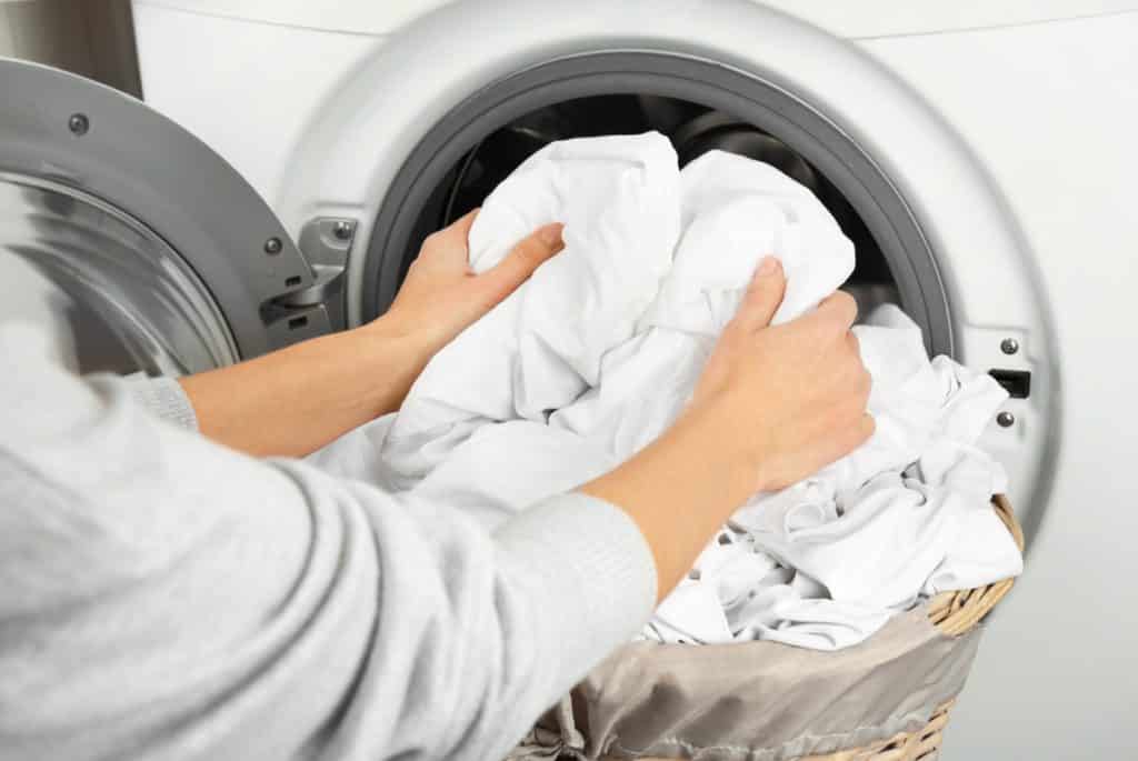 Hands putting sheets in a washing machine.