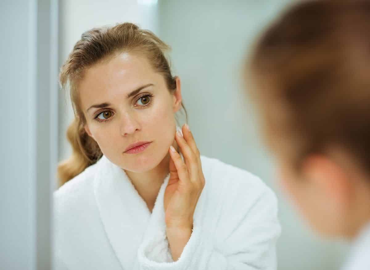a woman looks at her face in the mirror