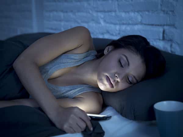 woman falls asleep with her phone next to her in bed