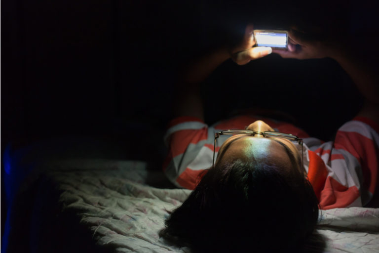 A child looks at their phone while lying in bed.