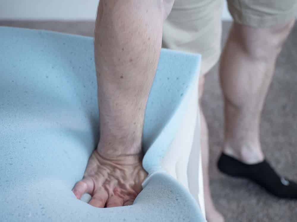 Man pressing down on foam layers in mattress