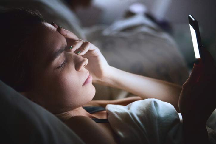 A Woman Looks At Her Phone In Bed