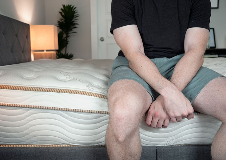 A man is sitting on an innerspring mattress.