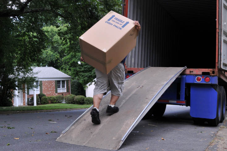 A man lifts a heavy box into a moving truck.