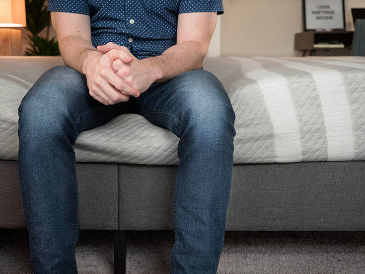 A man sits on the edge of a mattress.