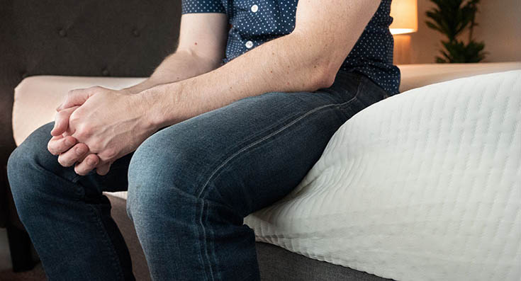 A man sits on the edge of his mattress.