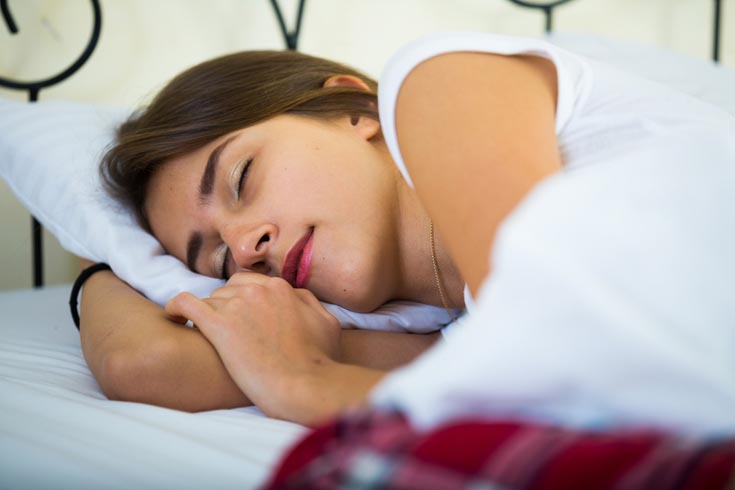 A teen sleeps under white sheets.