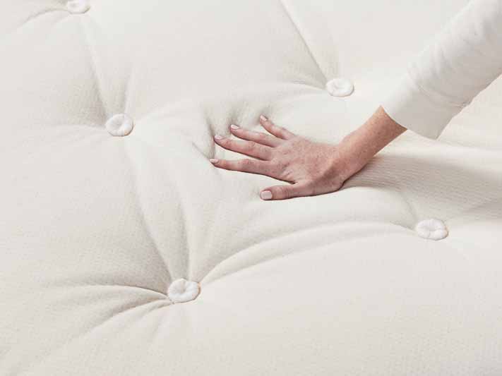 A woman places her hand on a mattress.