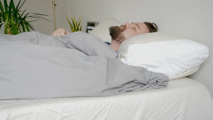 A man sleeps under a grey duvet.