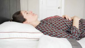 A woman rests on her back with the Saatva Latex Pillow.