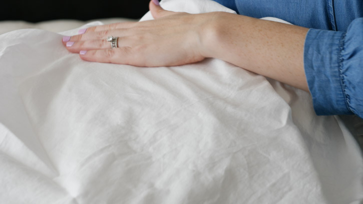 A hand feels the Saatva Organic sheets.