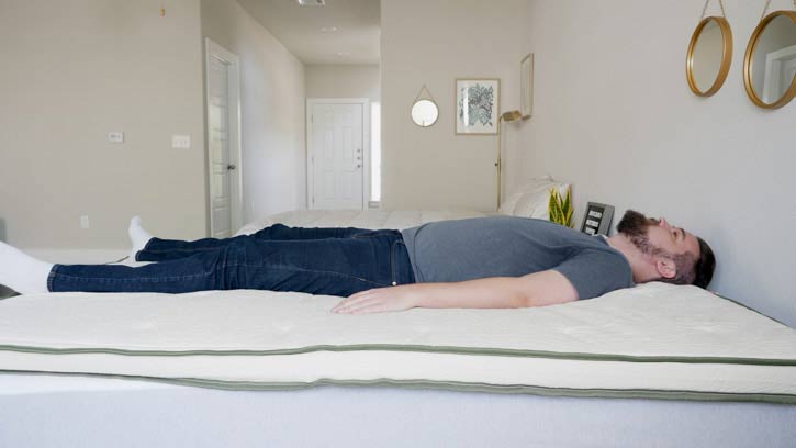 A man lies on his back on a mattress topper.