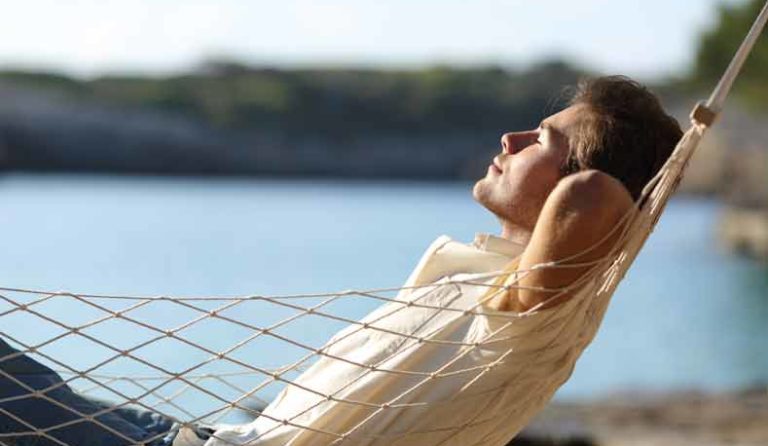 A man smiles and sleeps in a hammock.