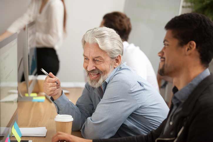 Two coworkers smile as they look at a computer screen.