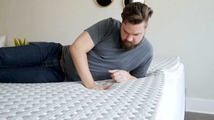 A man rests on the Layla foam topper, running his hand across it.