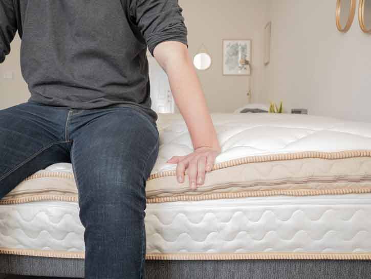 A man sits on the edge of a mattress.