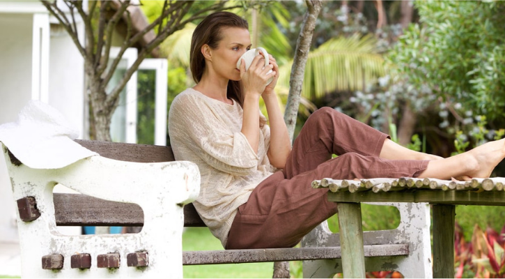 A woman drinks tea on a park bench