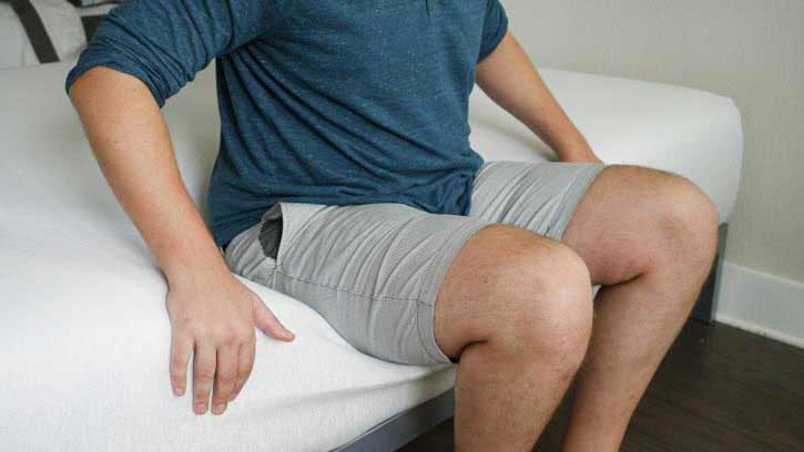 A man sits on the edge of a mattress.