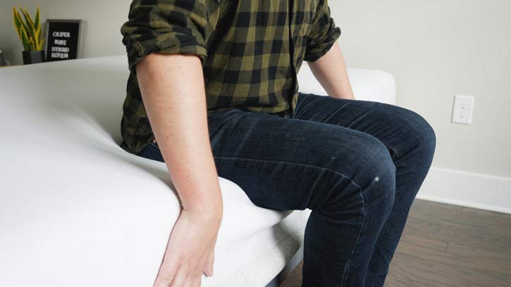 A man sits on the edge of a mattress.