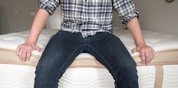 A man sits on the edge of his mattress.