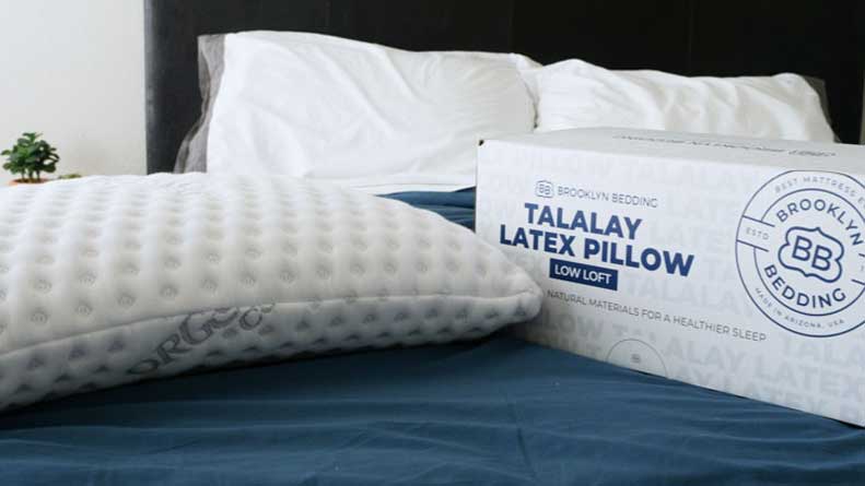 A Brooklyn Bedding Talalay Latex pillow and its box sit on a bed. 