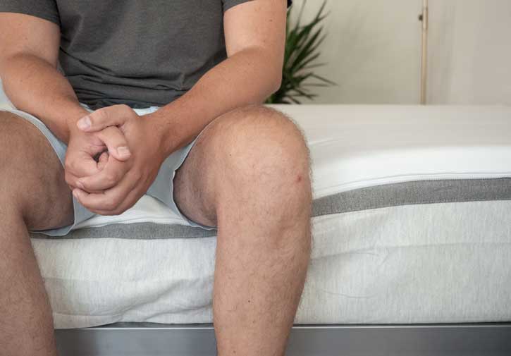 A man sits on the edge of his bed.