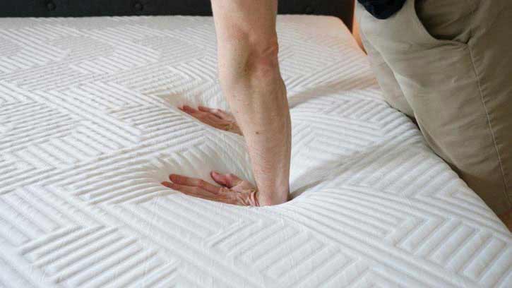 A man pushes into the top of a mattress.