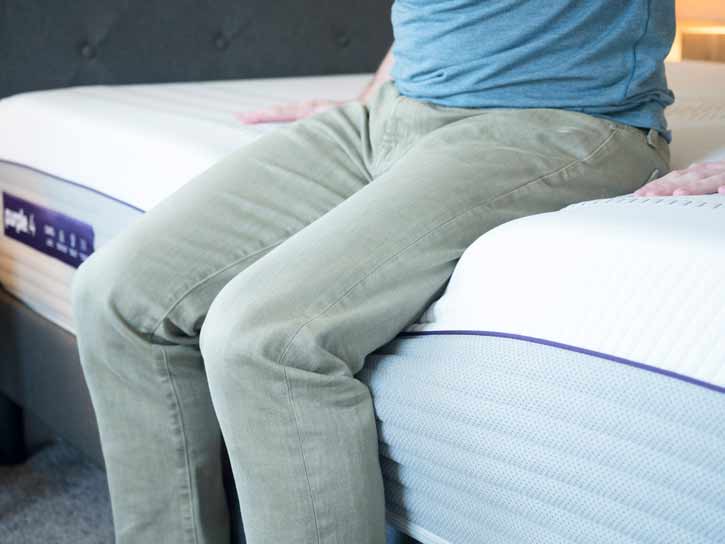 A man sits on the edge of his mattress.