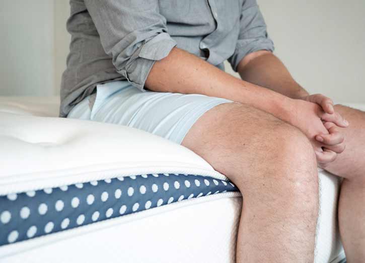 A man is sitting near the edge of a mattress.