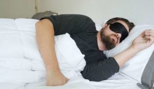 A man sleeps on his side while wearing a sleep mask.