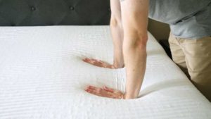 Two hands pushing down firmly on a mattress.