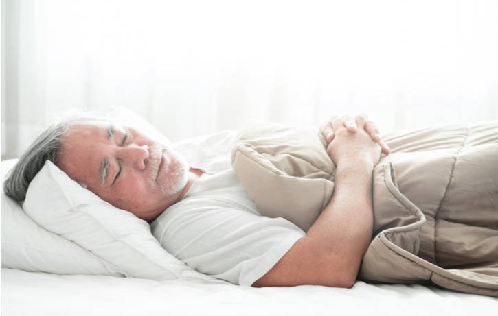 An elderly man sleeps on his back.