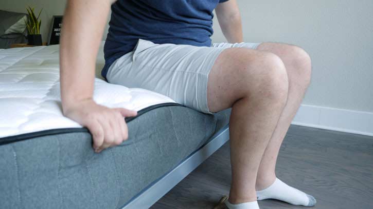 A man sits on the edge of a mattress