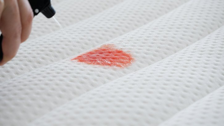 Eine Person reinigt einen Blutfleck von einer Matratze