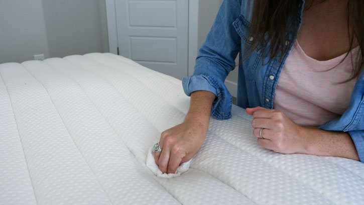 A woman cleans the top of a mattress